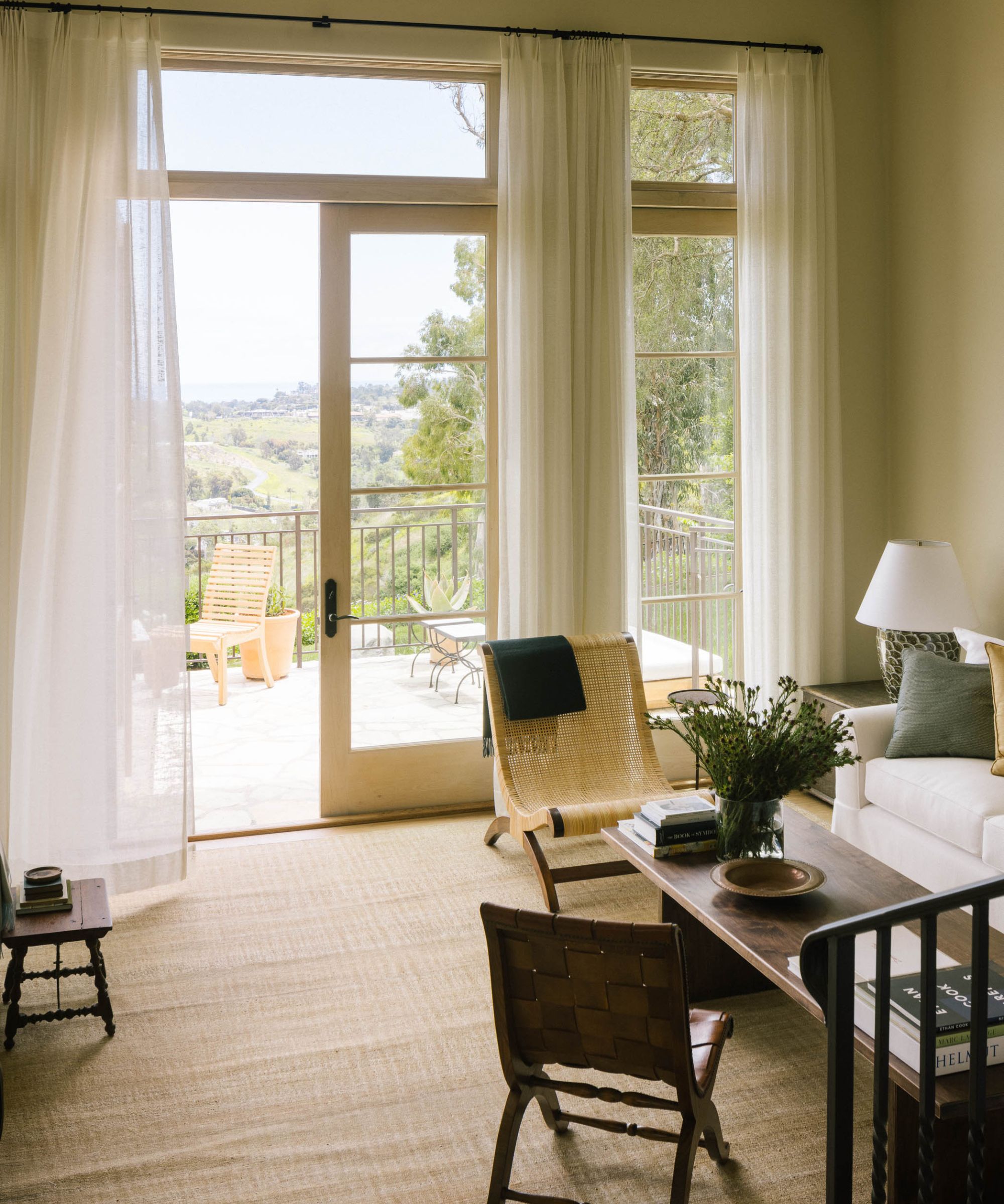 a neutral Spanish style living room with large patio doors looking out to a view of Malibu with a mix of vintage furnishings indoors