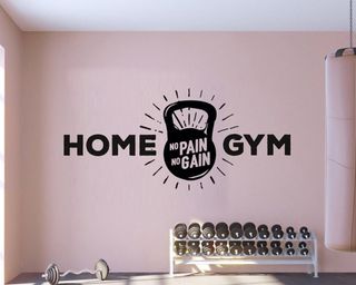 A home gym with pink wall paint decor, pink boxing bag and black wall decal with kettlebell, racked weights on floor