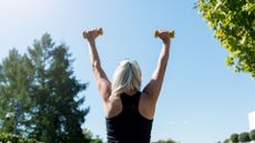 Woman lifting dumbbells above head while strength training in sunny park after working out how much weight should I lift