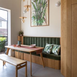 Wooden panelled breakfast nook in kitchen with green cushions.
