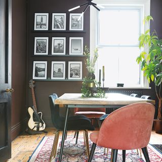 Brown dining room with table and chairs on rug and floating shelves with photos on wall