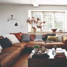 A living room with a large brown leather corner sofa with multi-coloured cushions and a glass-topped coffee table in the middle