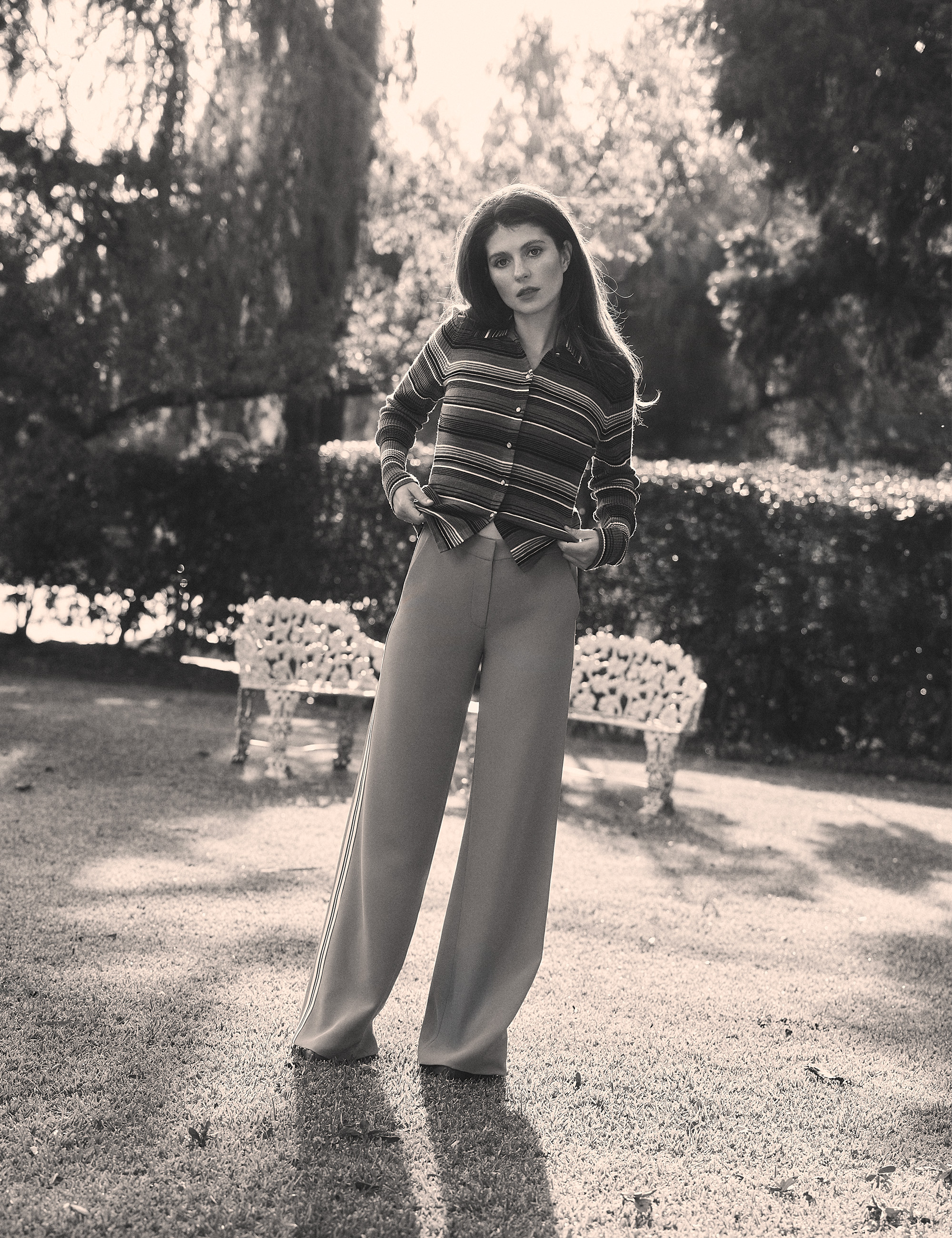 Emily Bader is photographed for Who What Wear's In Focus feature standing on the front lawn of a home. She is wearing a striped cardigan with wide-leg trousers.
