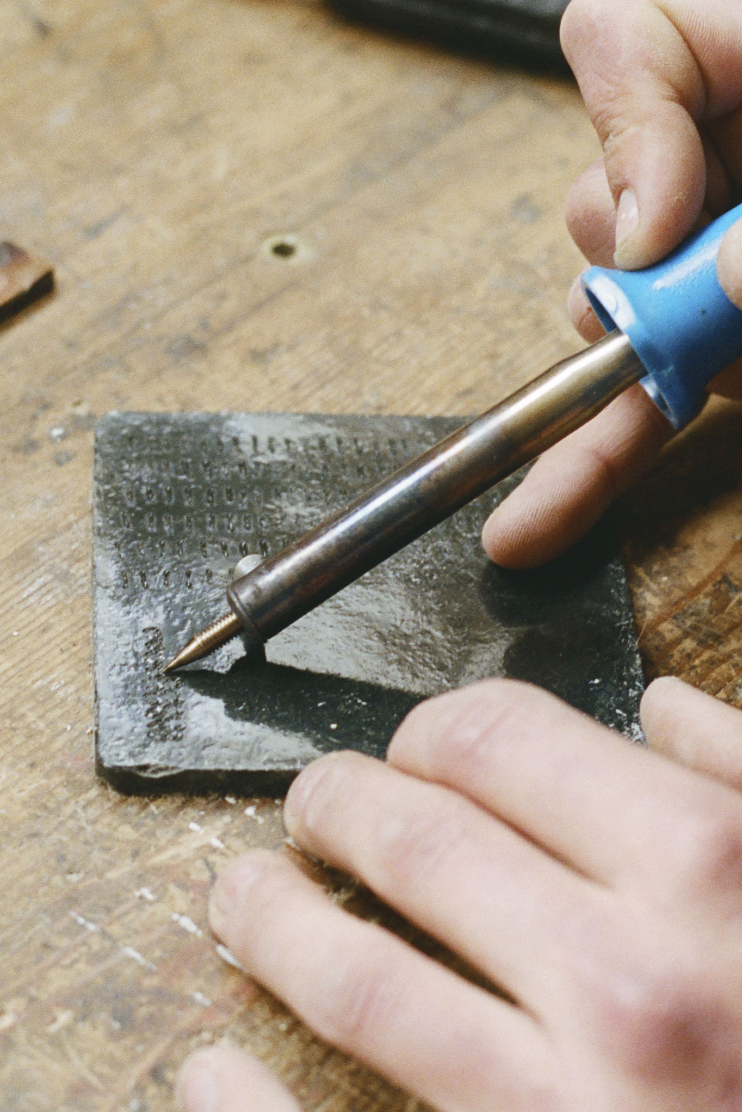 An artisan's hand inscribing a ceramic plaque on a workshop wooden table.
