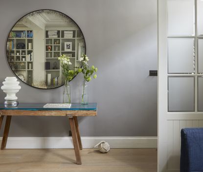 An entryway with a side table, two vases of flowers, and a round mirror