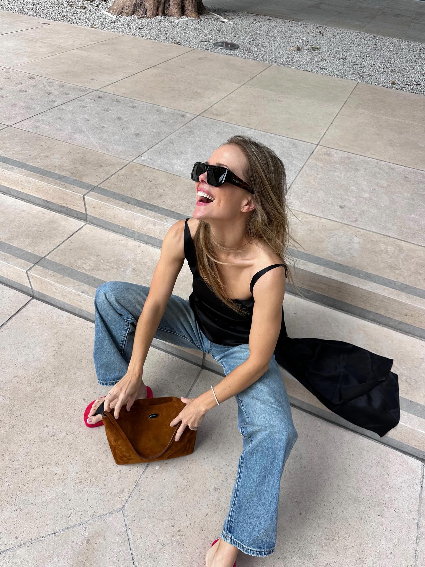 rachelle rowlings wears a black cami, blue jeans, flip flops and black sunglasses