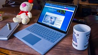 En Surface Laptop 4 står öppnad på ett skrivbord bredvid en kaffekopp, en nallebjörn och ett block, med TechRadar-hemsidan öppnad på skärmen.