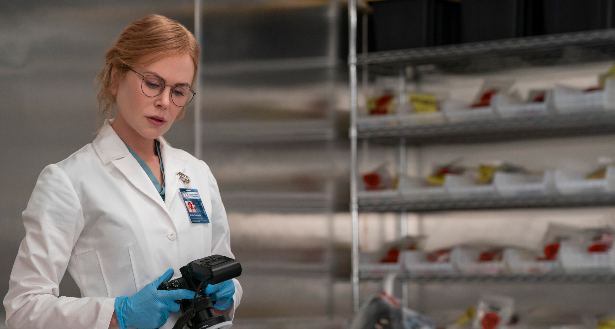 nicole kidman as kay scarpetta in a white labcoat and glasses examining a body in a still from prime video's scarpetta