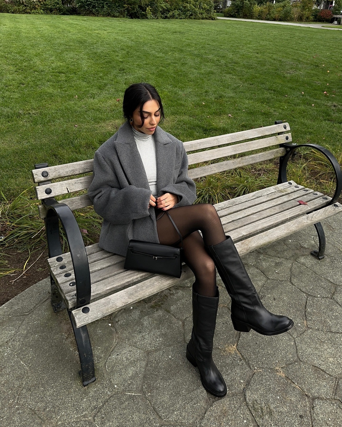 Mobina Peiman wears an oversized Oak and Fort jacket with black boots by Dolce Vita while sitting on a park bench.