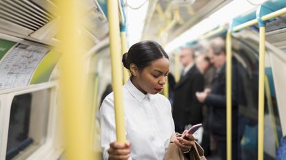 UK, London, businesswoman in underground train looking at cell phone