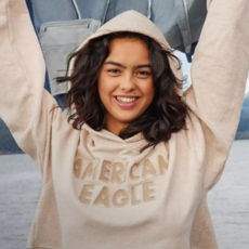 Young woman in cream American Eagle hoodie holding denim jacket in the air