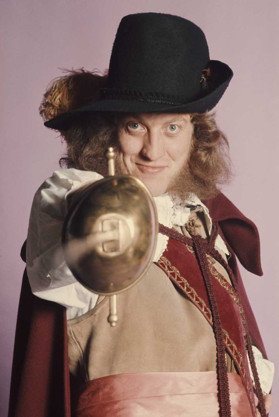 Singer Noddy Holder, of English glam rock group Slade, posing in a cavalier costume and pointing a sword, London, 1974