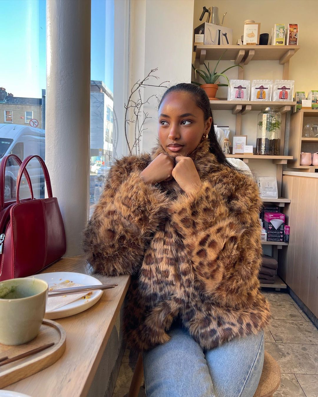 Rayan wears a leopard-print faux-fur coat with blue jeans and a red shoulder bag.