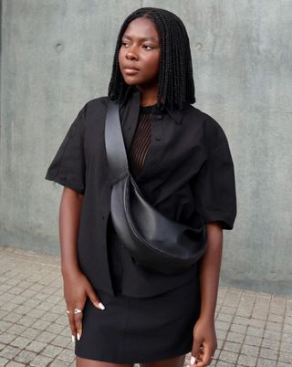 Woman wears black shirt, black crossbody bag, black skirt