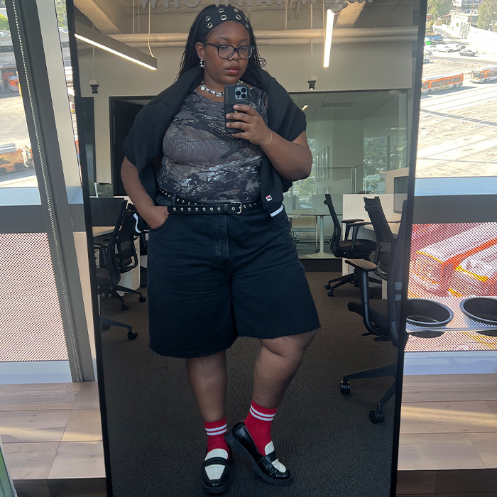 chichi wears camo top, long black denim shorts, grommet belt, black and white loafers, red socks, a black grommet headband, and a black sweatshirt over her shoulders