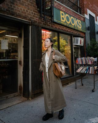 Erica Choi wearing a chic fall outfit with a long trench coat, brown leather tote, and black boots in New York City.