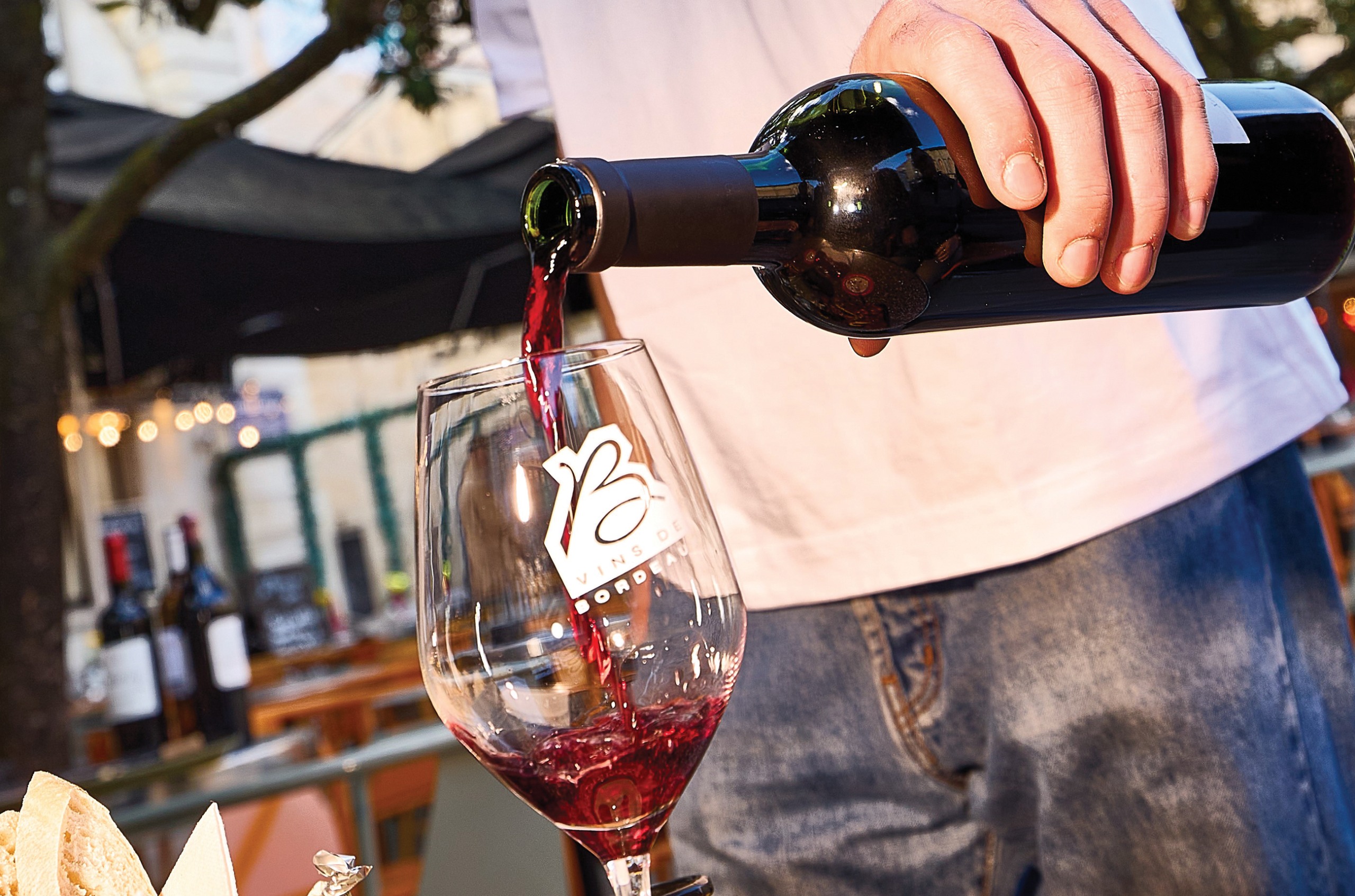A hand pouring red wine into a glass with 'Bordeaux' on it