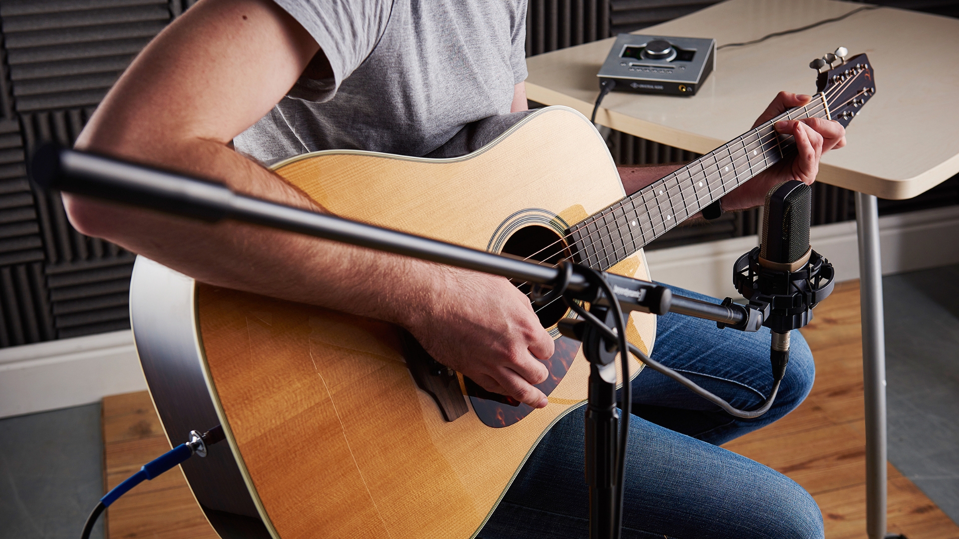 A man plays acoustic guitar with a condenser microphone plugged into an audio interface