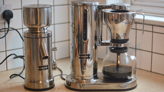 Image of the Aarke Coffee System – a stainless steel coffee bean grinder and drip coffee maker – positioned on a kitchen counter