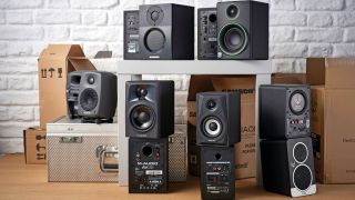 A selection of budget studio monitors on the floor and table with their boxes scattered around the room