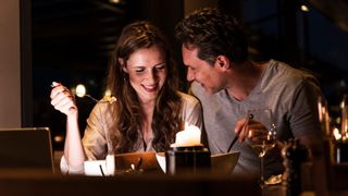 Romantic couple sitting together over candlelit dinner holding forks and drinking wine, representing a rebound relationship