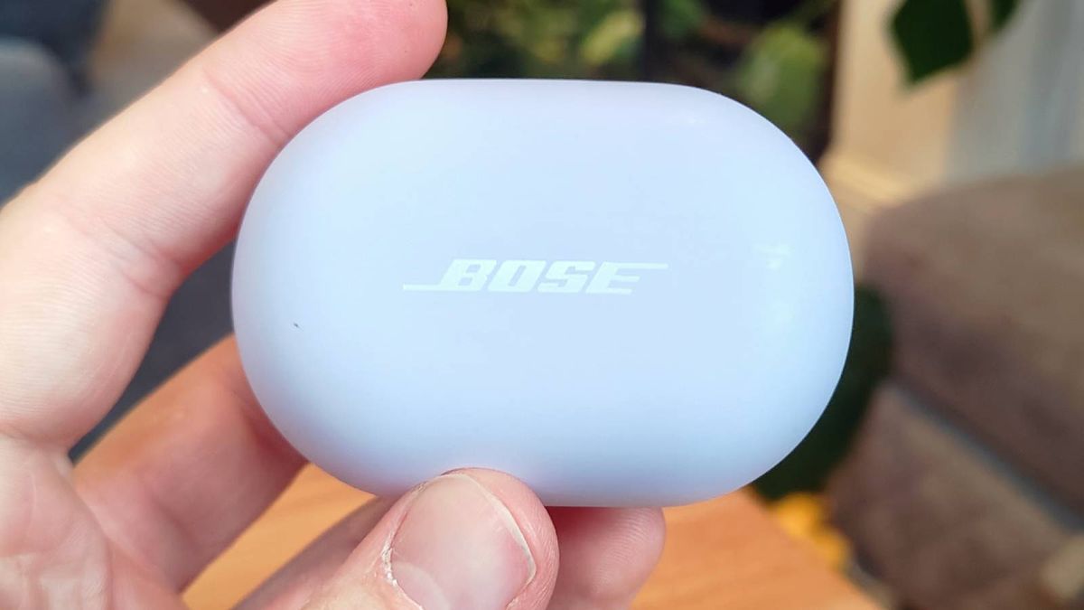 The Bose QuietComfort Earbuds 2024 held above a wooden table.