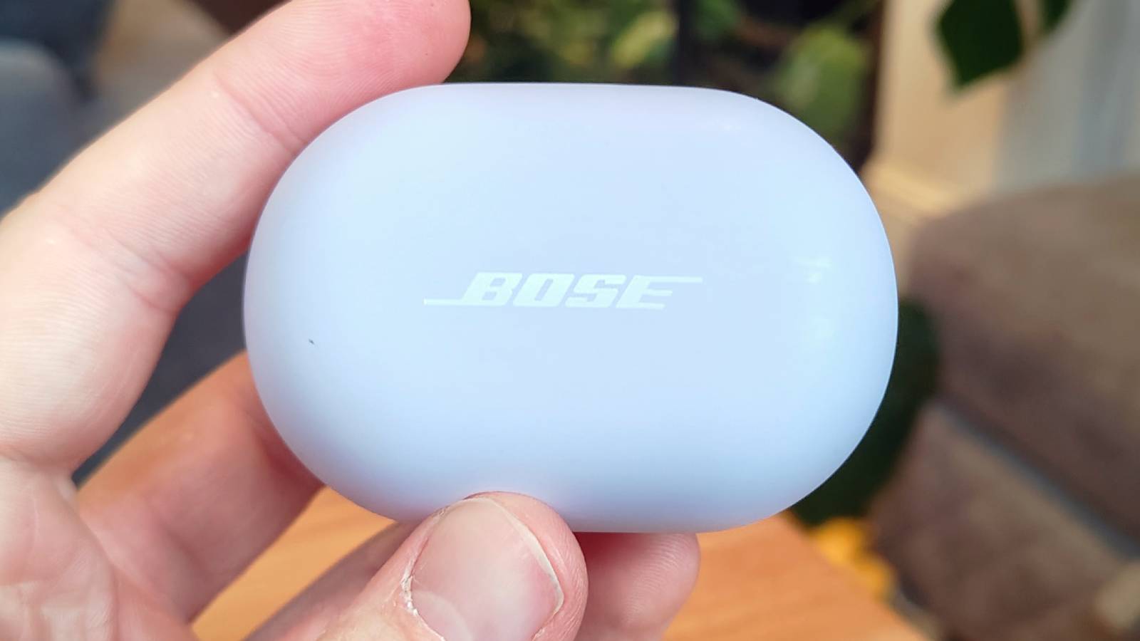 The Bose QuietComfort Earbuds 2024 held above a wooden table.