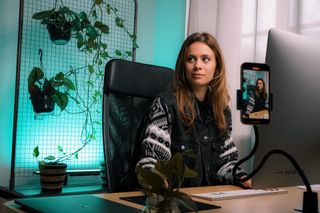 Female content creator filming herself on a mobile phone behind a desk