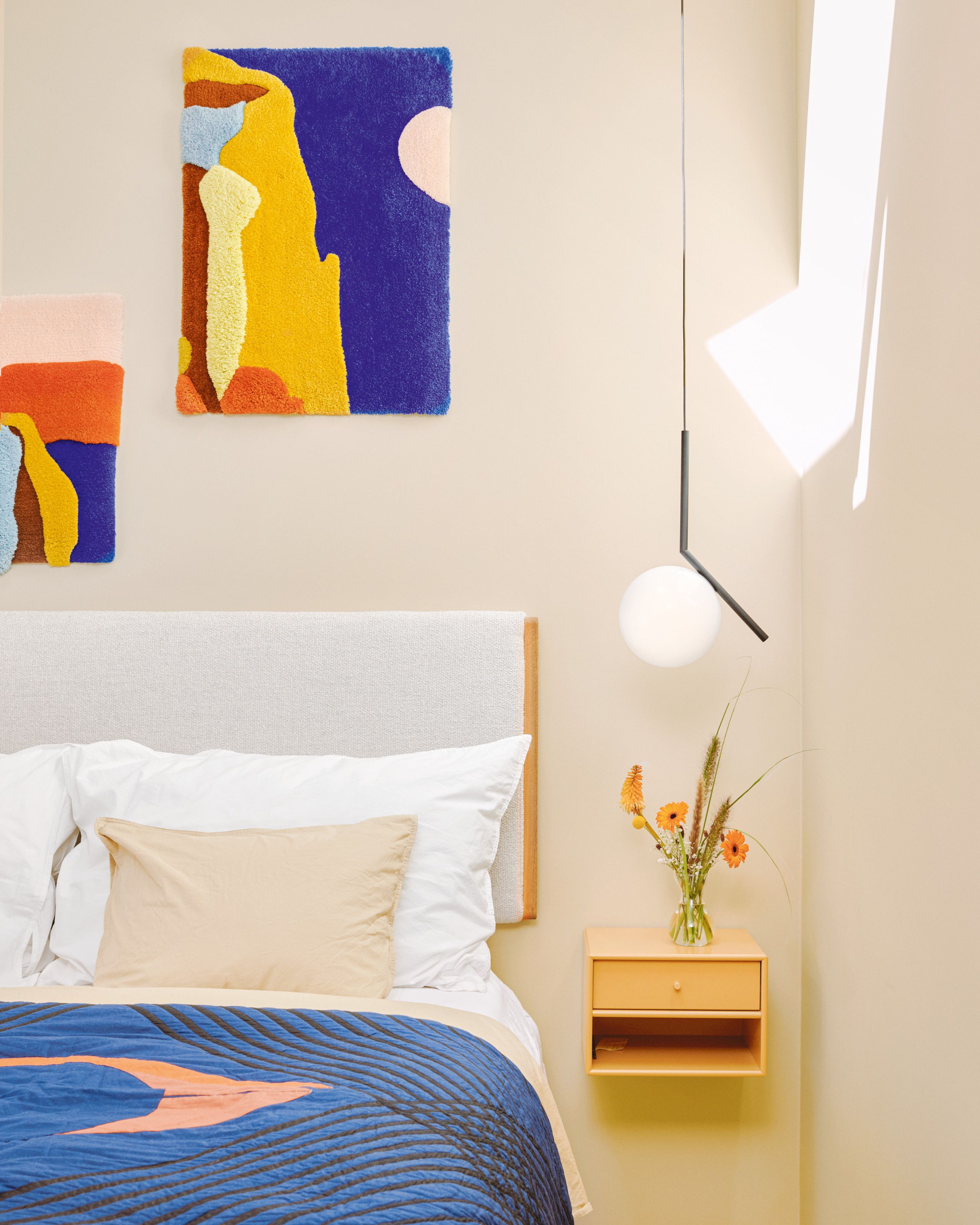 Off-white bedroom with white upholstered walls, wall-hung wood side table, textured abstract artwork