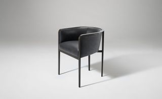 A black suede tub shaped chair with thin legs