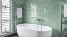 Mint green bathroom with metro tiles on the walls and a white oval freestanding bath and two heated towel rails