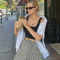 woman wearing striped pants, black tank, and grey sweater over shoulders