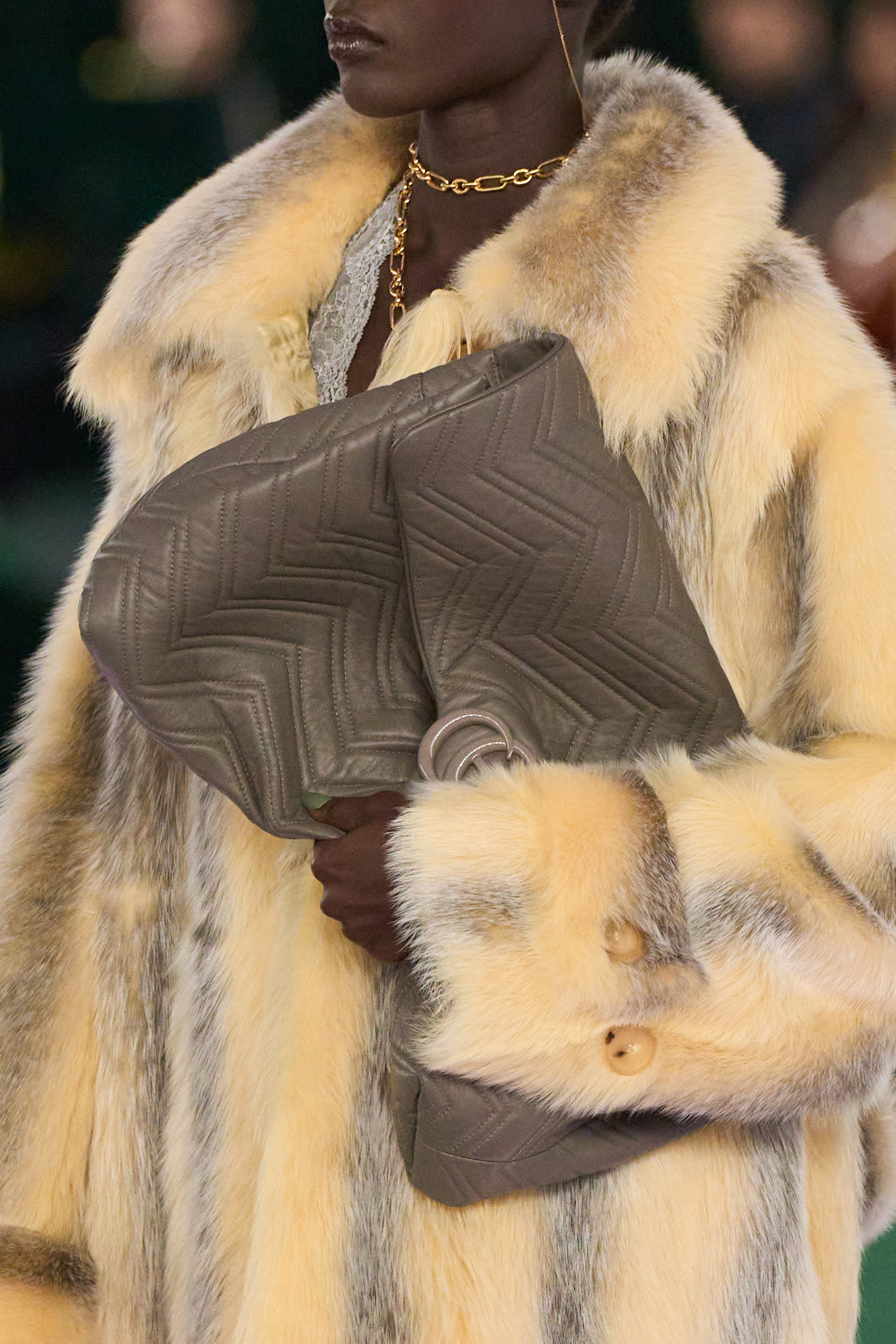 a woman on the Gucci Fall 2025 runway in a yellow and gray fur coat carrying a gray quilted clutch purse