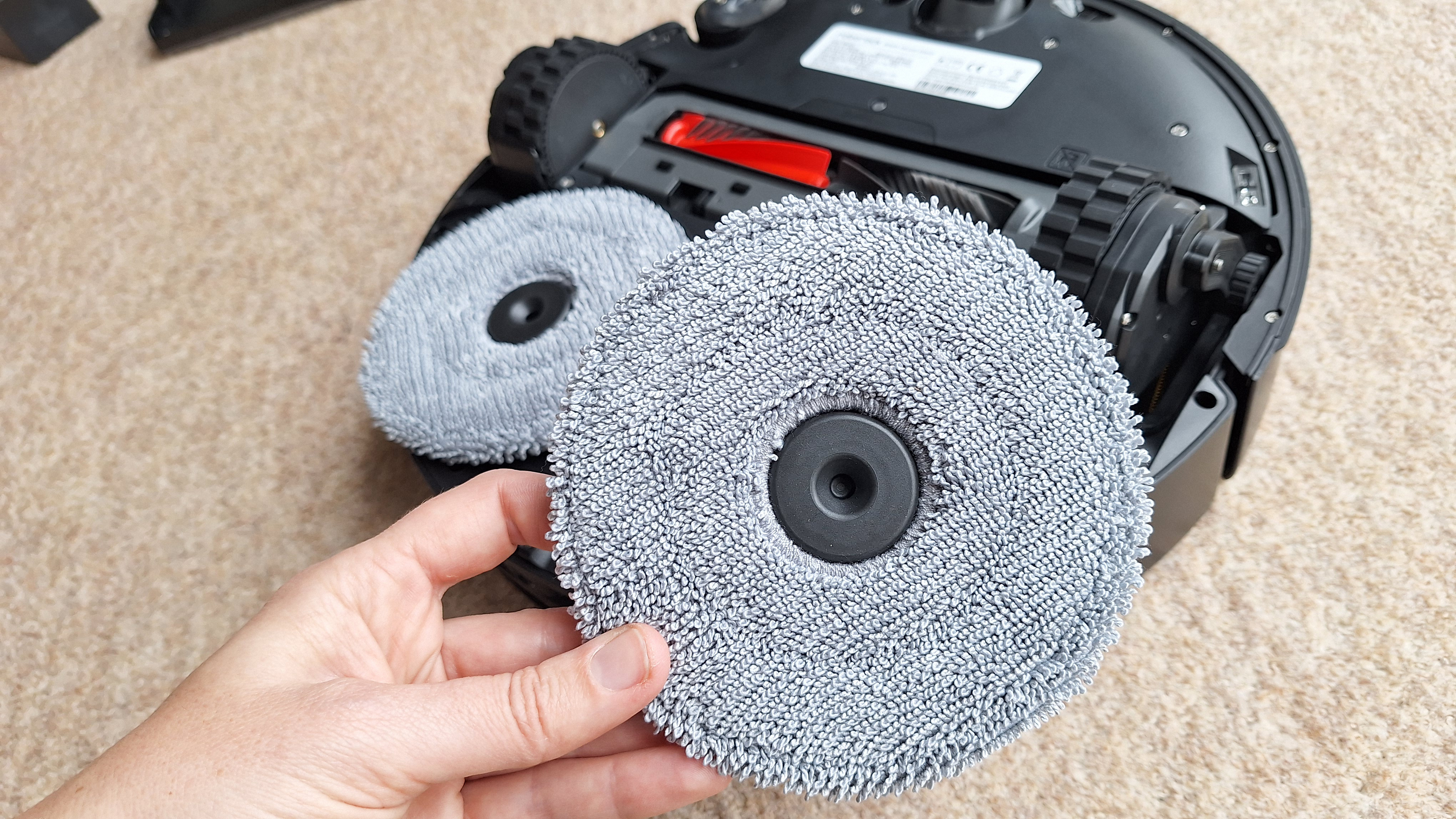 Roborock Saros 20 robot vacuum flipped over to show mop pads, with one removed and held in tester's hand