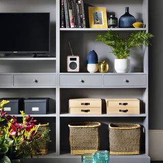 Grey painted shelving unit with baskets, books, television and ornaments painted the same colours as a grey wall