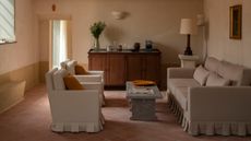 Beige, soft pink, and ochre yellow living room. There is a skirted sofa with two skirted accent chairs across from each other. There is a stone coffee table in between the two seating areas. 