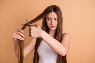 A woman with long hair is cutting is with scissors.