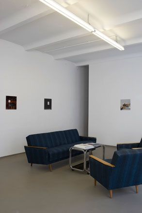 Interior room, grey floor, white walls, blue sofa, two armchairs, small silver frame coffee table, pictures on the wall