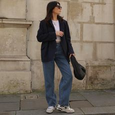 Influencer Francesca Saffari wears Levi jeans, a blazer, and white tee with New Balance sneakers and a woven black bag. 