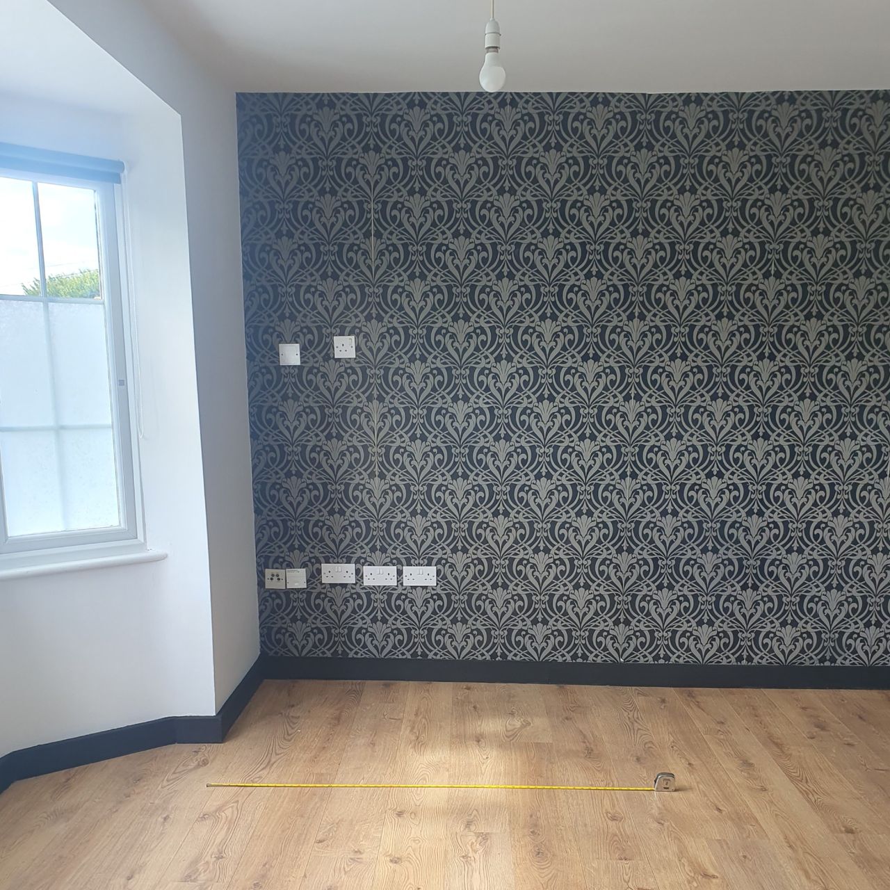 The before: An empty studio flat with white walls, matt black skirting boards and a feature wall covered in a black and grey wallpaper