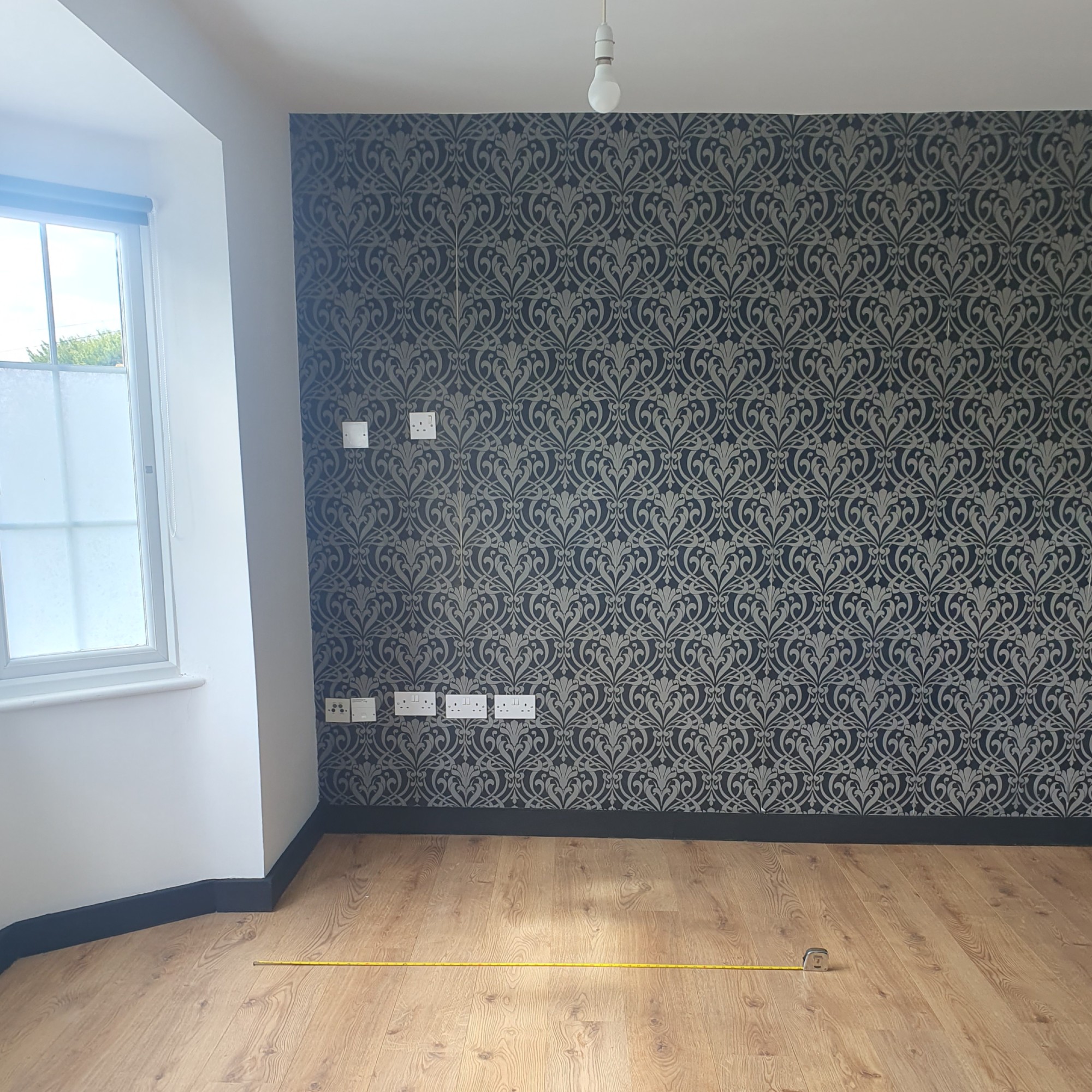 The before: An empty studio flat with white walls, matt black skirting boards and a feature wall covered in a black and grey wallpaper