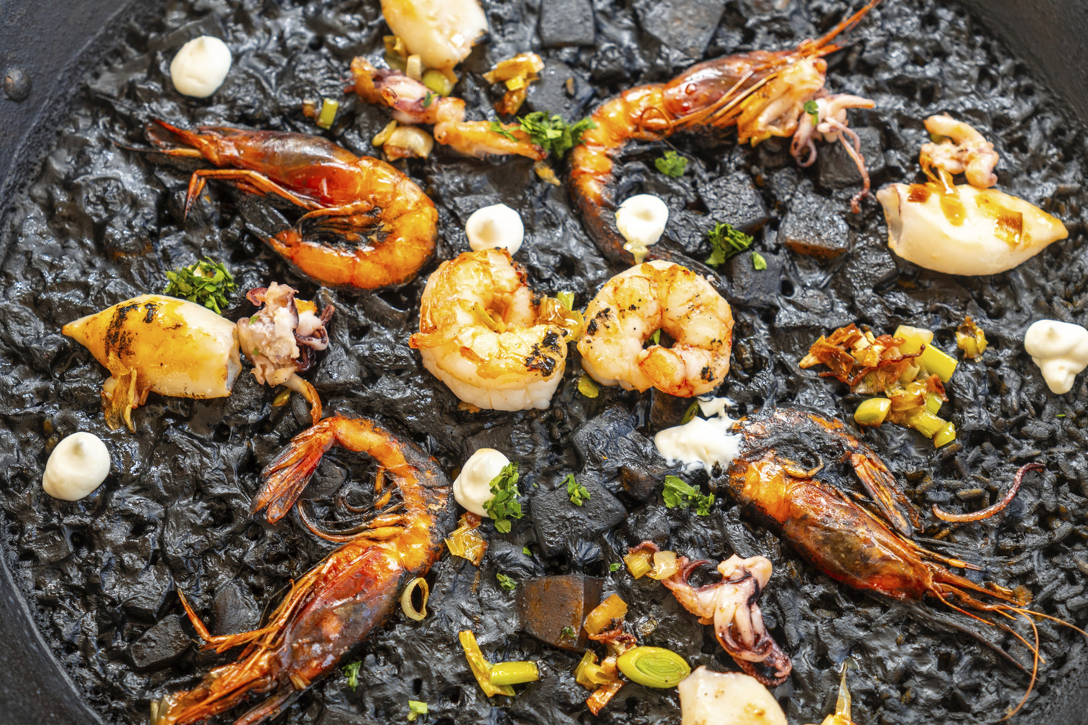 Close up of black rice paella with grilled shrimps, squid, and aioli