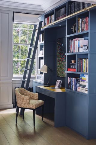 Study with built in book shelving and desk in blue, desk chair, wood floor and window with blind