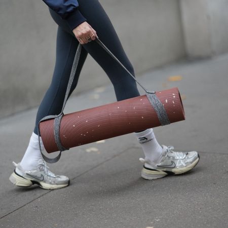 woman carrying rolled up exercise mat wearing black leggings and nike trainers