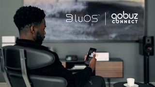 Qobuz Connect and BluOS logos on a background next to a man looking at a mobile phone