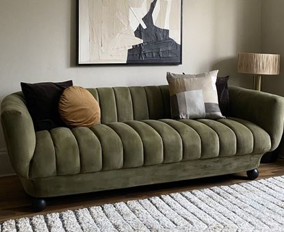 A living room with a green velvet sofa and a neutral colored rug