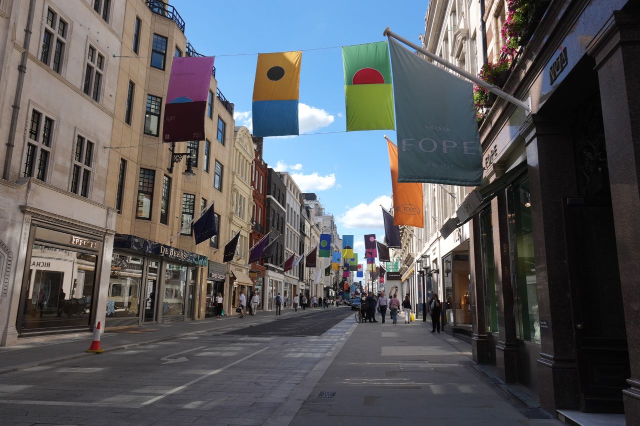 Bond Street in London lined with luxury stores and colorful banners suspended above the road.