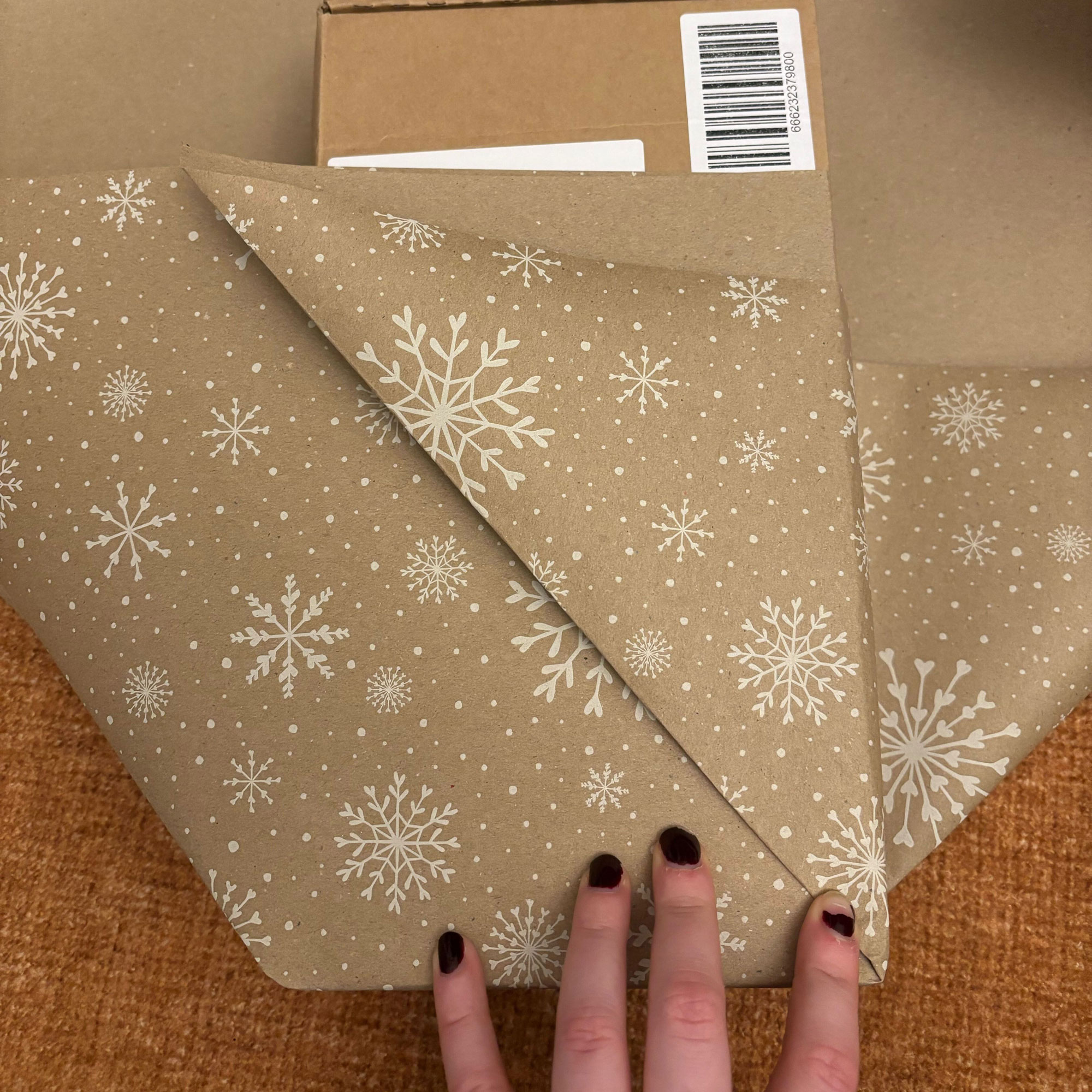 A rectangular box wrapped in brown paper with a white snowflake print on it