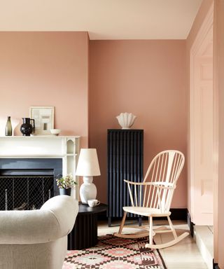 Pink living room, tonal palette of pinks used on ceiling and walls, ercol white rocking chair, geometric printed pink rug, white stone fireplace, cream sofa