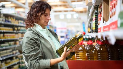 Woman in a grocery comparing prices of different olive oil bottles